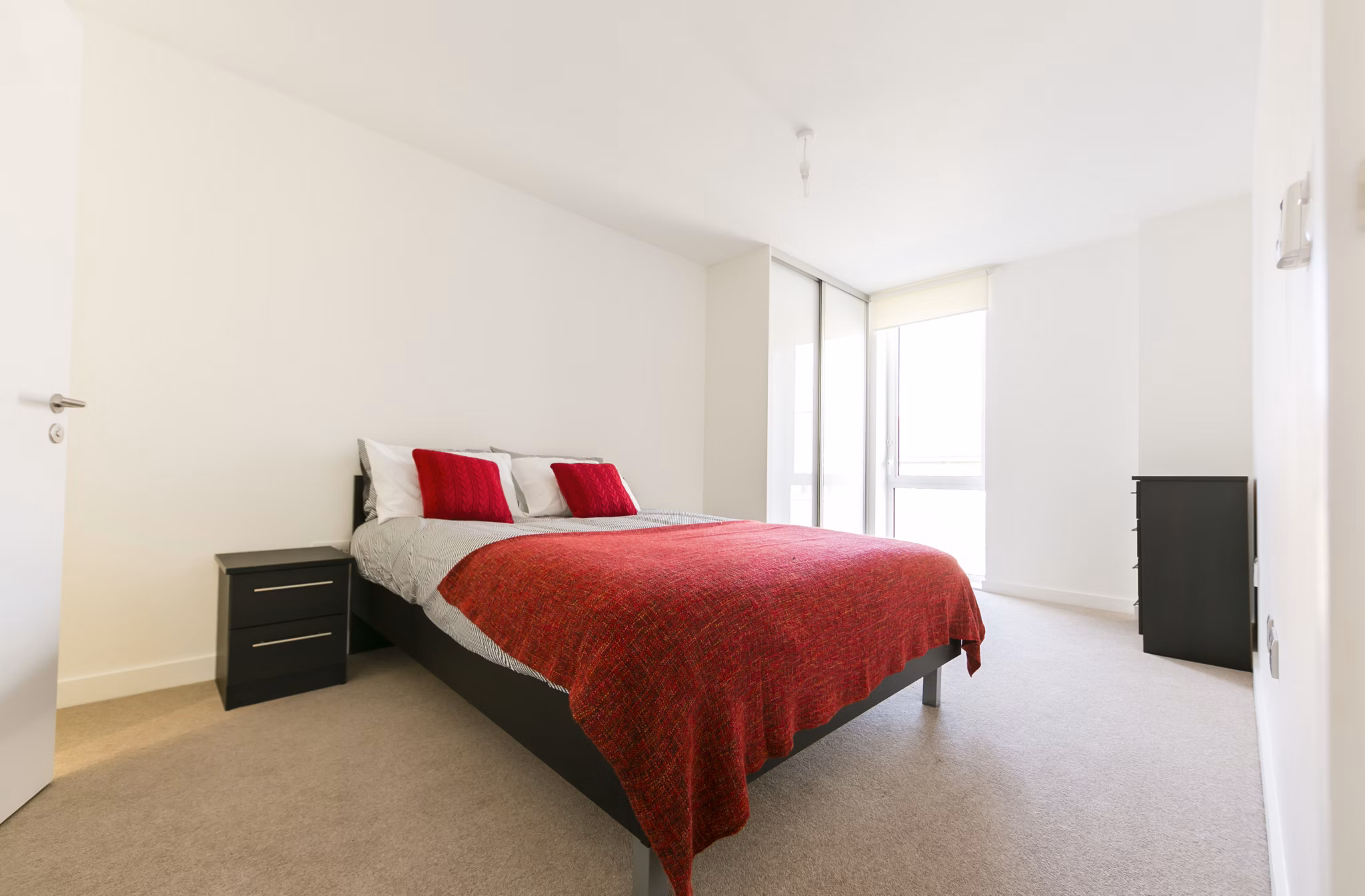 Bright and minimalist bedroom at Fizzy Stepney Green with a red blanket, modern furniture, and ample natural light.