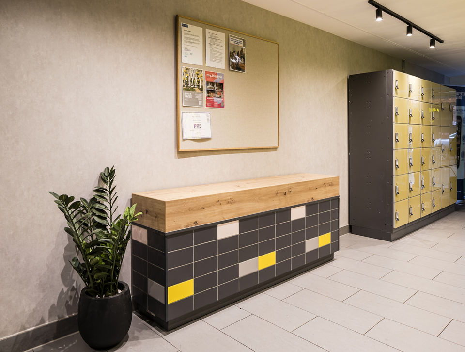 Cozy corner in the Fizzy Stepney Green lobby with yellow and gray lockers and decorative greenery.