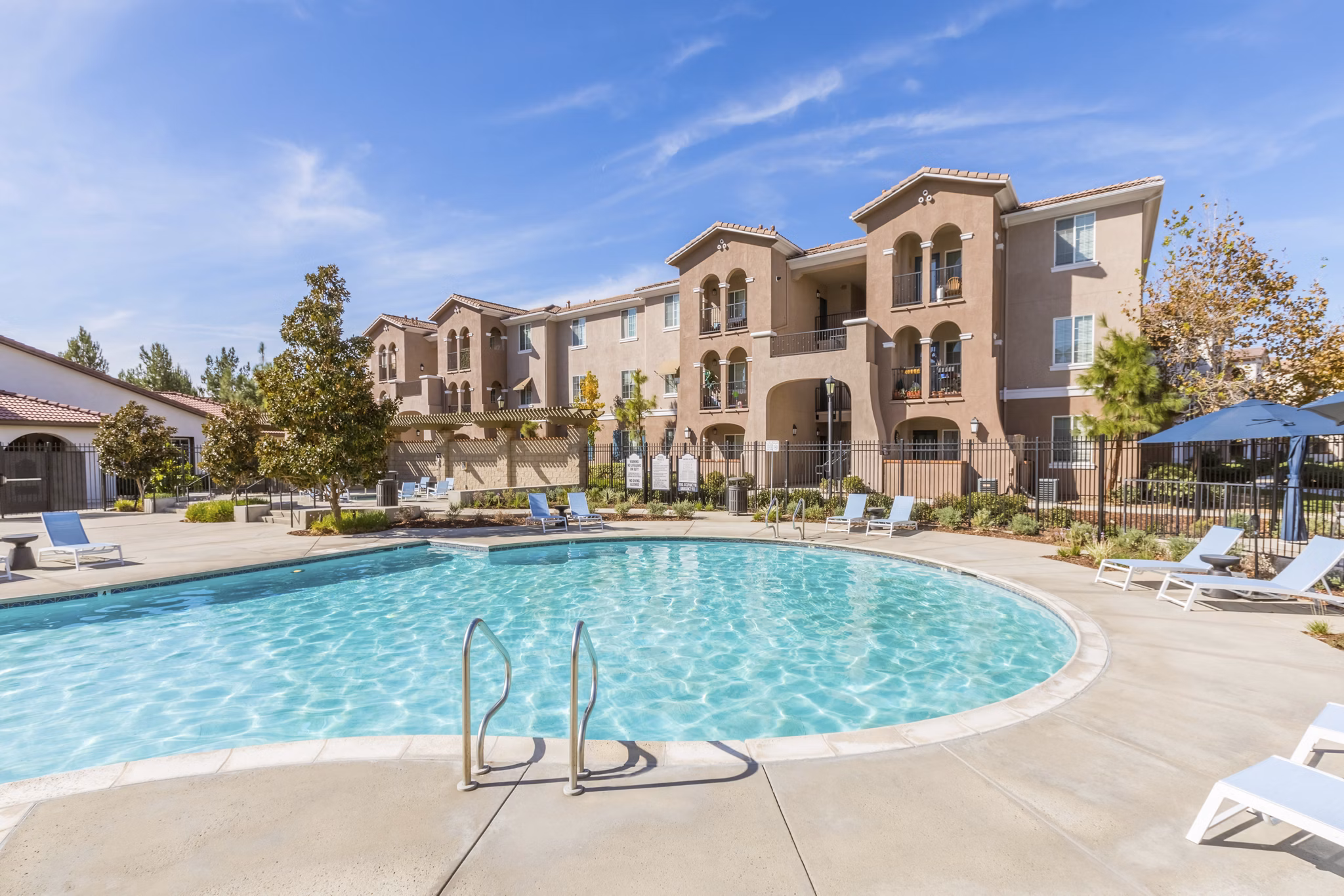 Resort-style pool area at Viano at Riverwalk Apartments featuring lounge chairs and lush landscaping
