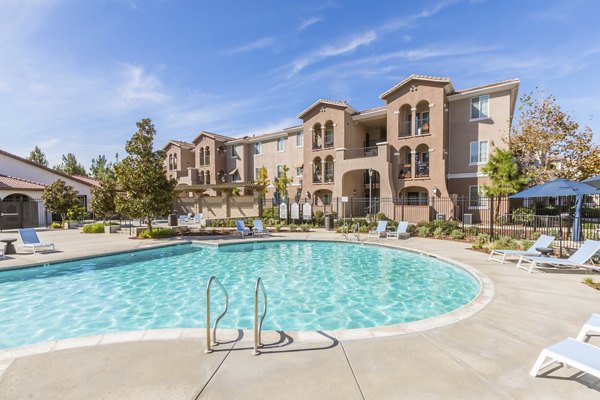 Resort-style pool area at Viano at Riverwalk Apartments featuring lounge chairs and lush landscaping
