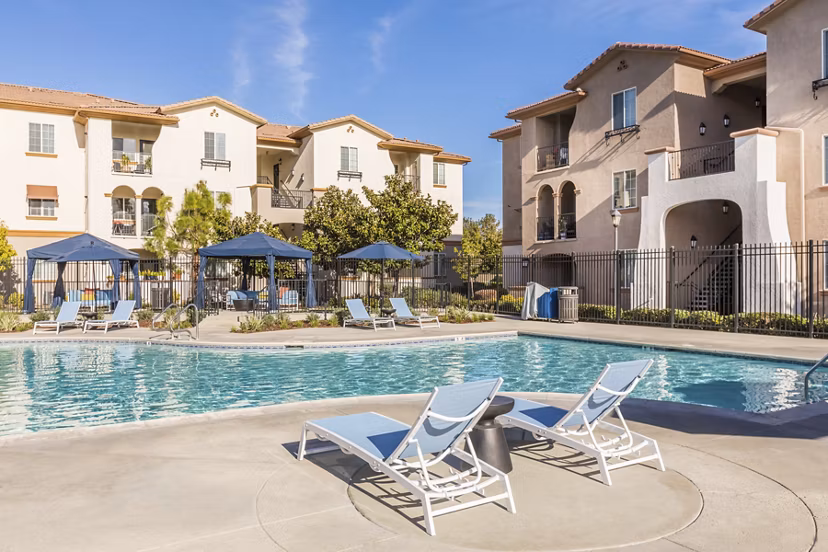 Resort-style pool at Viano at Riverwalk Apartments featuring lounge areas and lush landscaping
