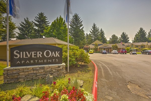 Entrance to Silver Oak Apartments featuring a welcoming sign and parking area with cars