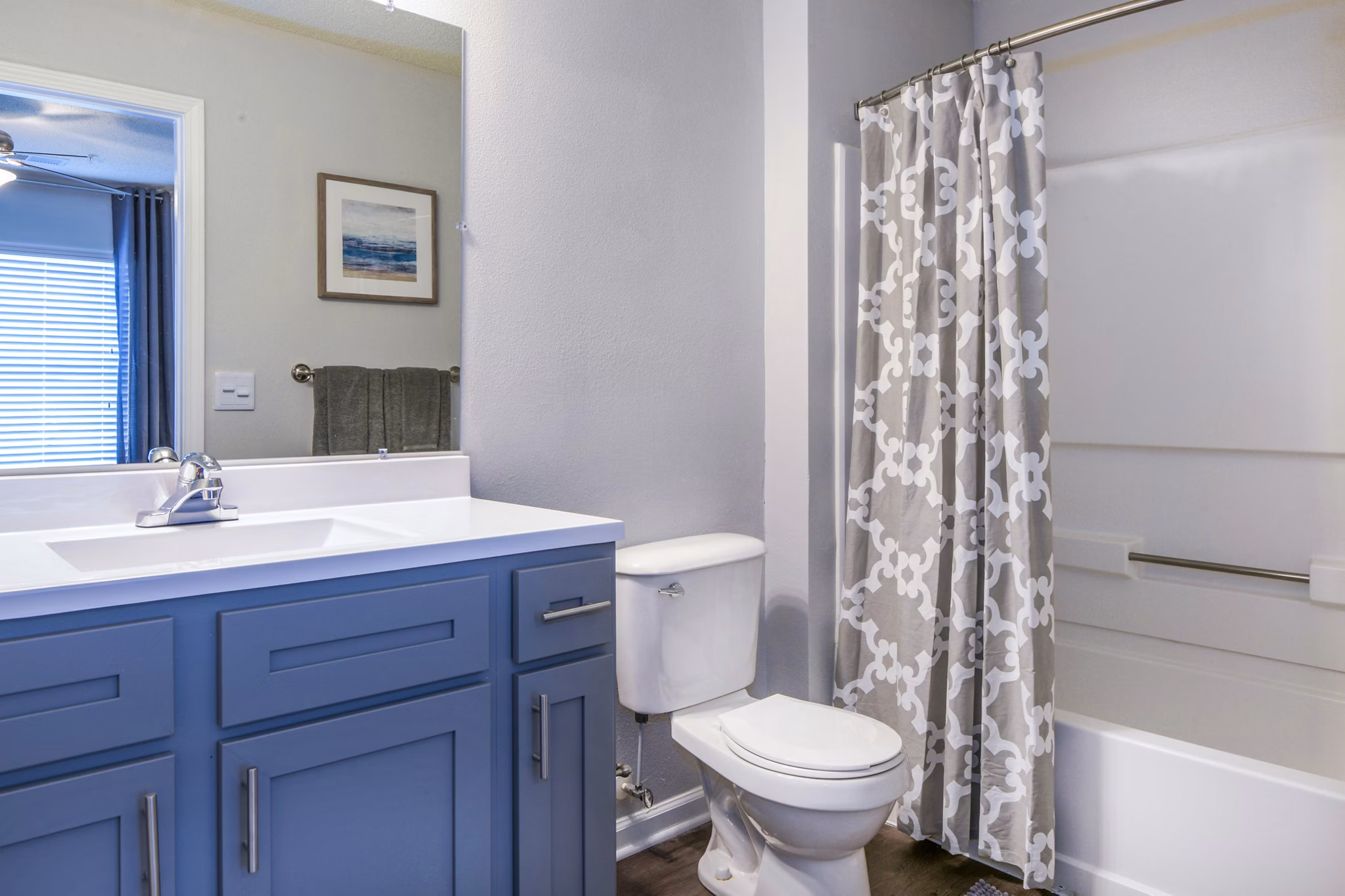 Modern bathroom featuring a blue vanity, sink, toilet, and bathtub with shower curtain in luxury apartment