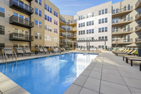 Resort-style pool at The Cynwyd Apartments featuring lounge chairs and palm trees