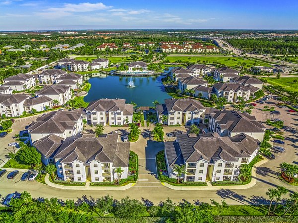 Aerial view of luxury apartments surrounding a serene pond with lush landscaping and winding roads