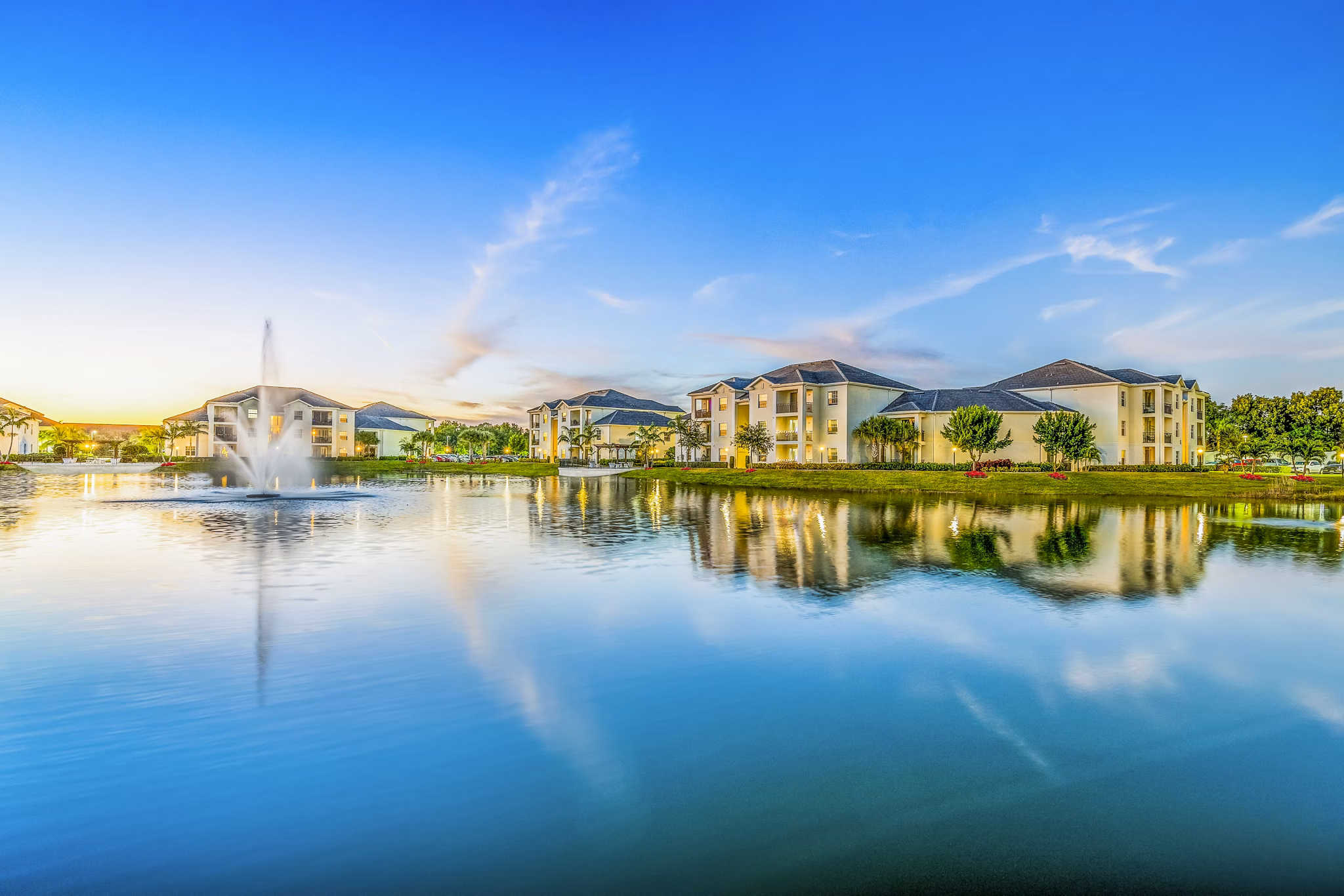 Serene lake view with fountain and residential buildings under a clear blue sky