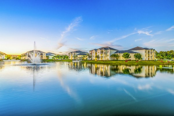 Serene lake view with fountain and residential buildings under a clear blue sky