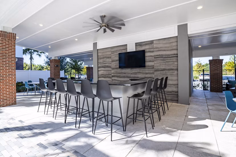 Outdoor pool patio at The Accolade Collegiate Village West Apartments with modern lounge chairs and lush landscaping