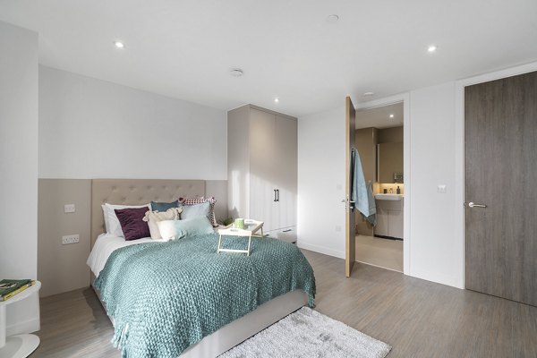 Bright and cozy bedroom at Canvas Coventry City Club in Coventry, featuring a teal bedspread, plush cushions, and an ensuite bathroom with modern fixtures.