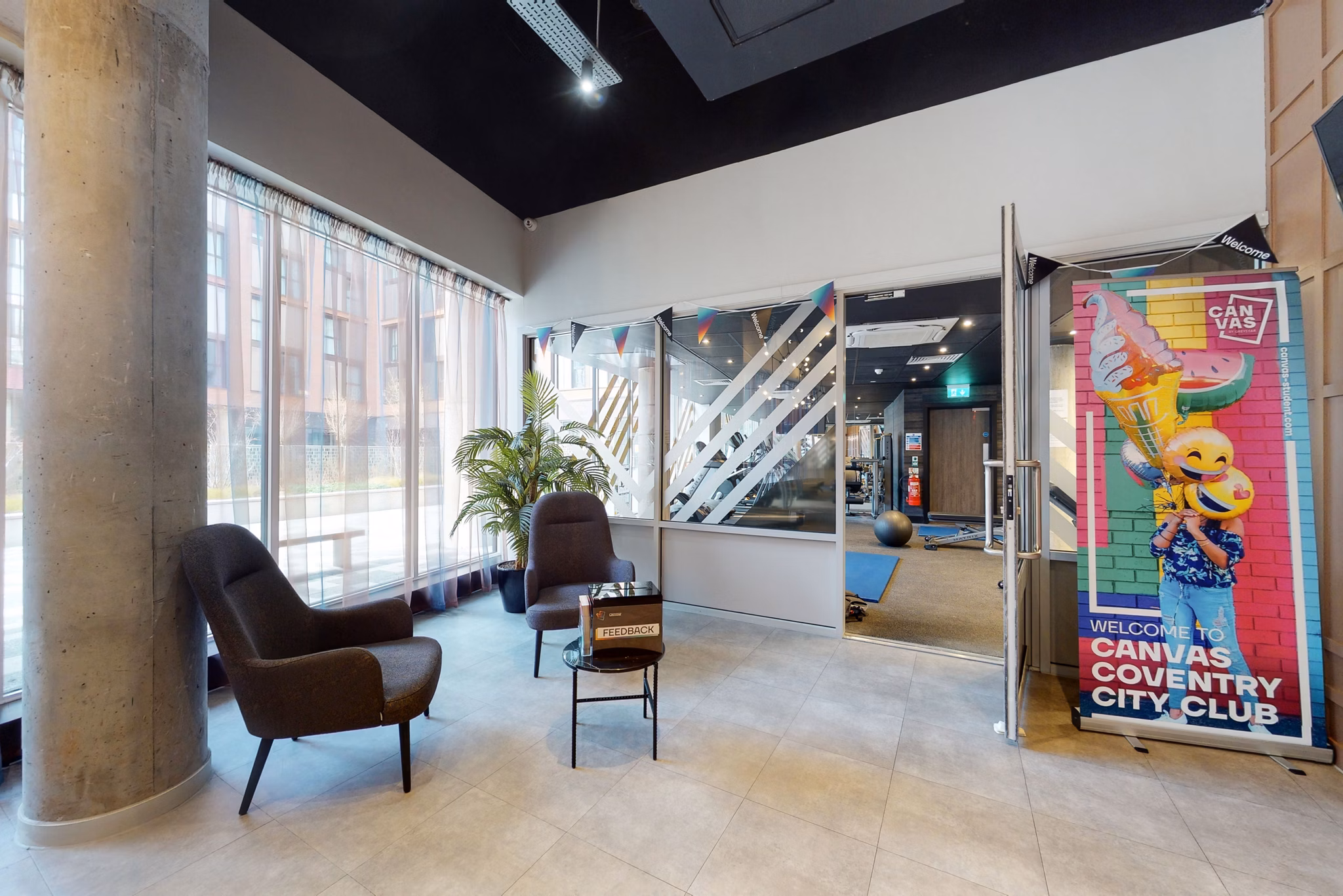 Welcoming lobby area at Canvas Coventry City Club in Coventry, featuring modern seating, floor-to-ceiling windows, and a vibrant promotional sign.