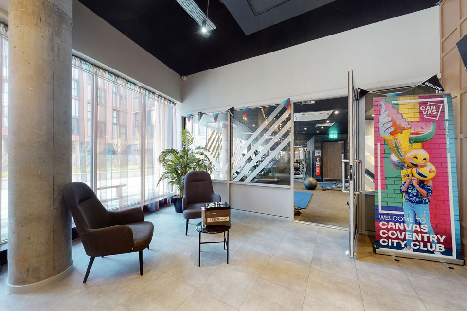 Welcoming lobby area at Canvas Coventry City Club in Coventry, featuring modern seating, floor-to-ceiling windows, and a vibrant promotional sign.
