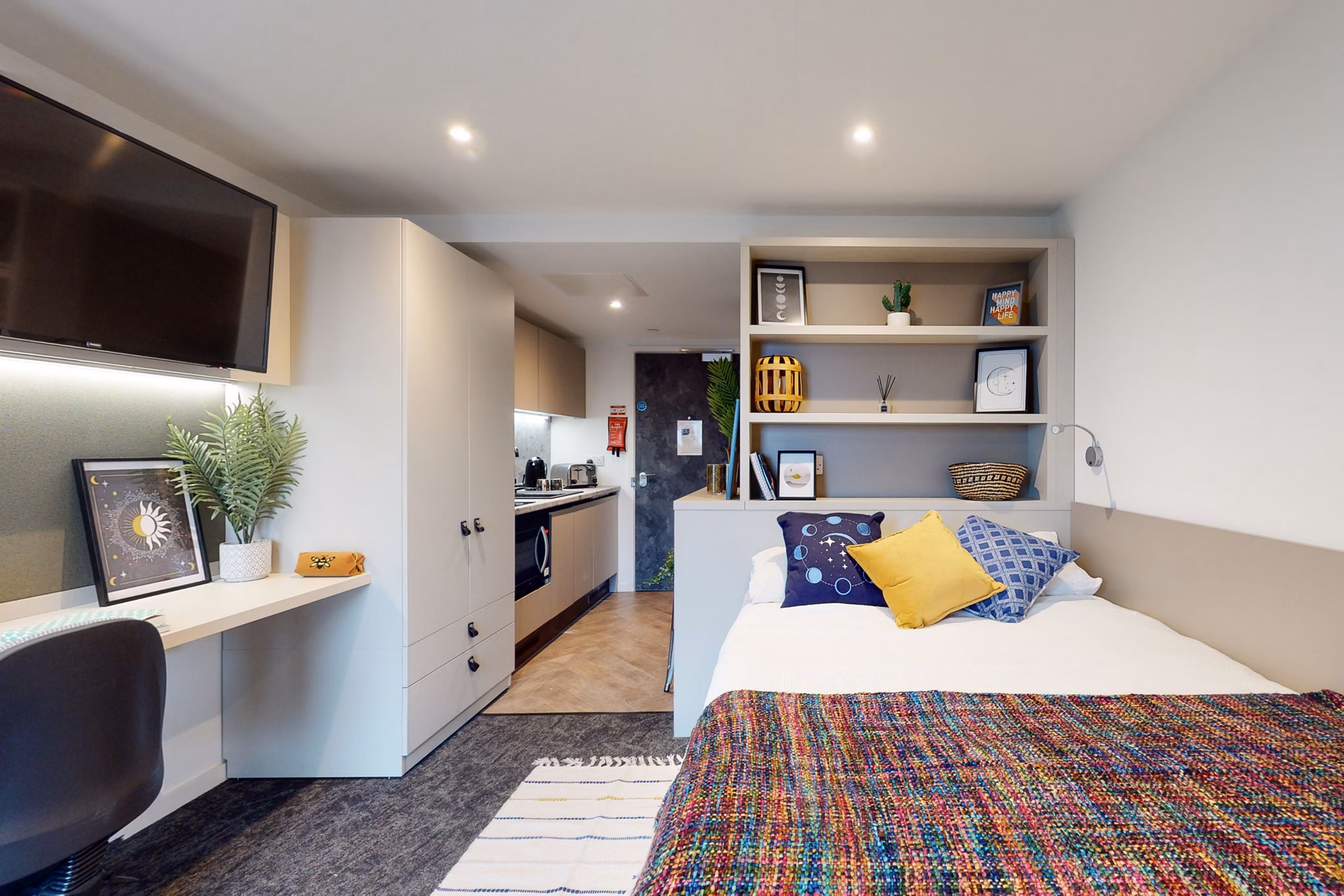 Interior shot of a Canvas Manchester apartment featuring a stylish bedroom with built-in shelving, a study desk, and a cozy bed with colorful bedding.