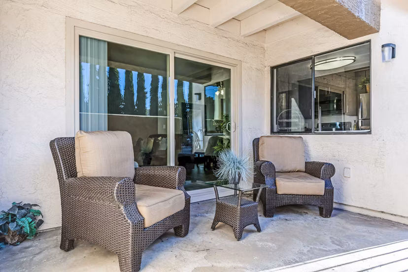 Patio area with wicker chairs and a small table, leading to the interior of luxury apartments