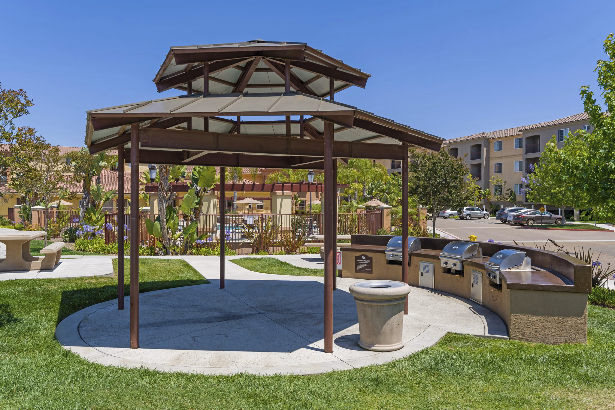 Outdoor grill area at Greenfield Village Apartments with modern seating and lush landscaping