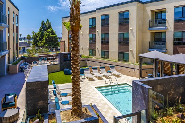 Poolside relaxation area at The Lofts at Carlsbad Village Apartments featuring lounge chairs and lush greenery Perfect for unwinding in luxury