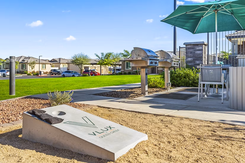 Outdoor BBQ grill area at Vlux at Queen Creek Apartments featuring modern seating and lush landscaping for recreational enjoyment