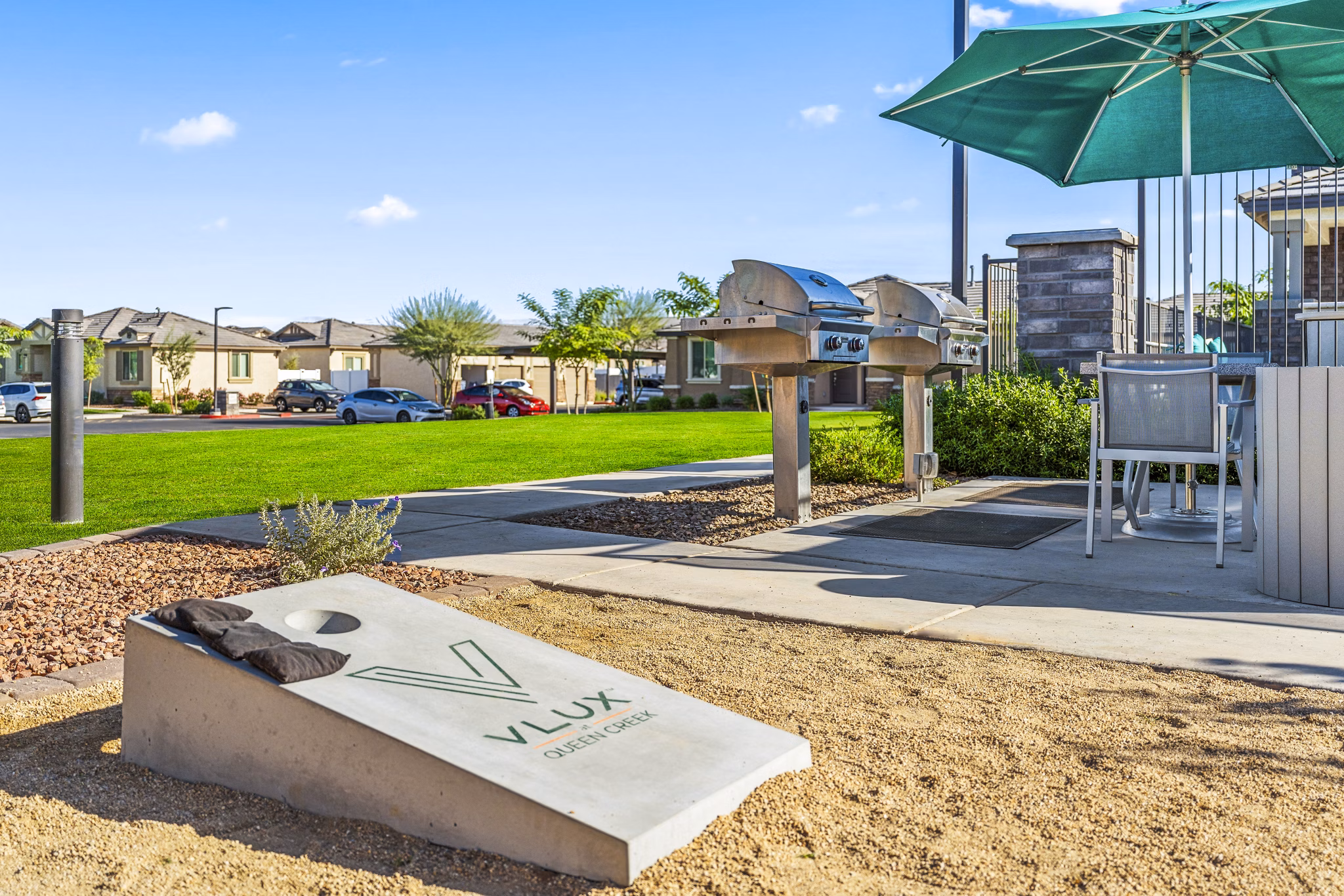Outdoor BBQ grill area at Vlux at Queen Creek Apartments featuring modern seating and lush landscaping for recreational enjoyment