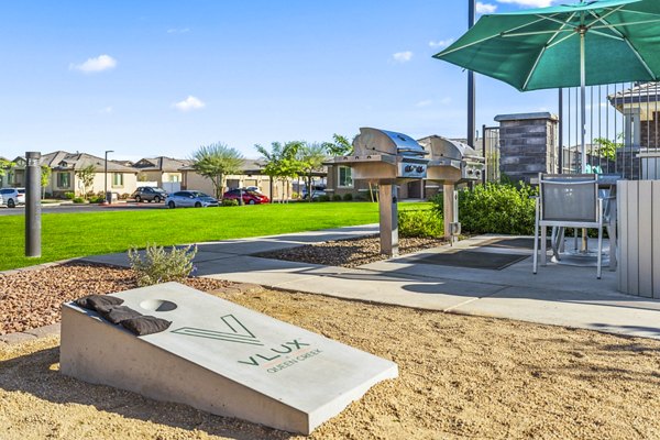 Outdoor BBQ grill area at Vlux at Queen Creek Apartments featuring modern seating and lush landscaping for recreational enjoyment