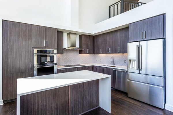 Contemporary kitchen featuring stainless steel appliances and marble countertops at The Travis Apartments