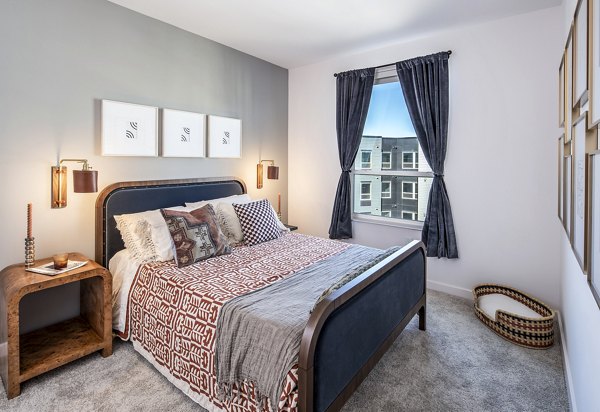 The Lucie Apartments: Stylish bedroom with patterned bedding, wall art, and large window