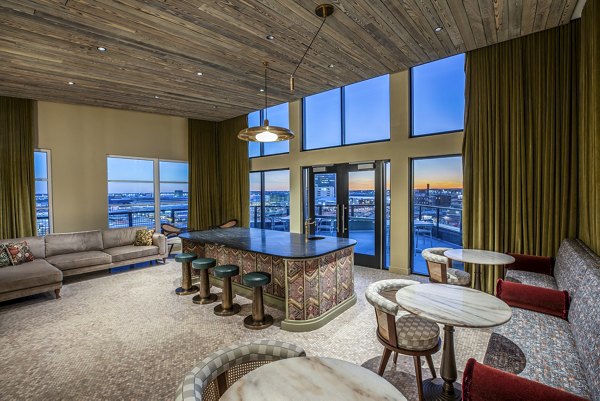 Modern lounge with bar, ample seating, large windows, and scenic city view at The Lucie Apartments Luxurious space for relaxation and socializing