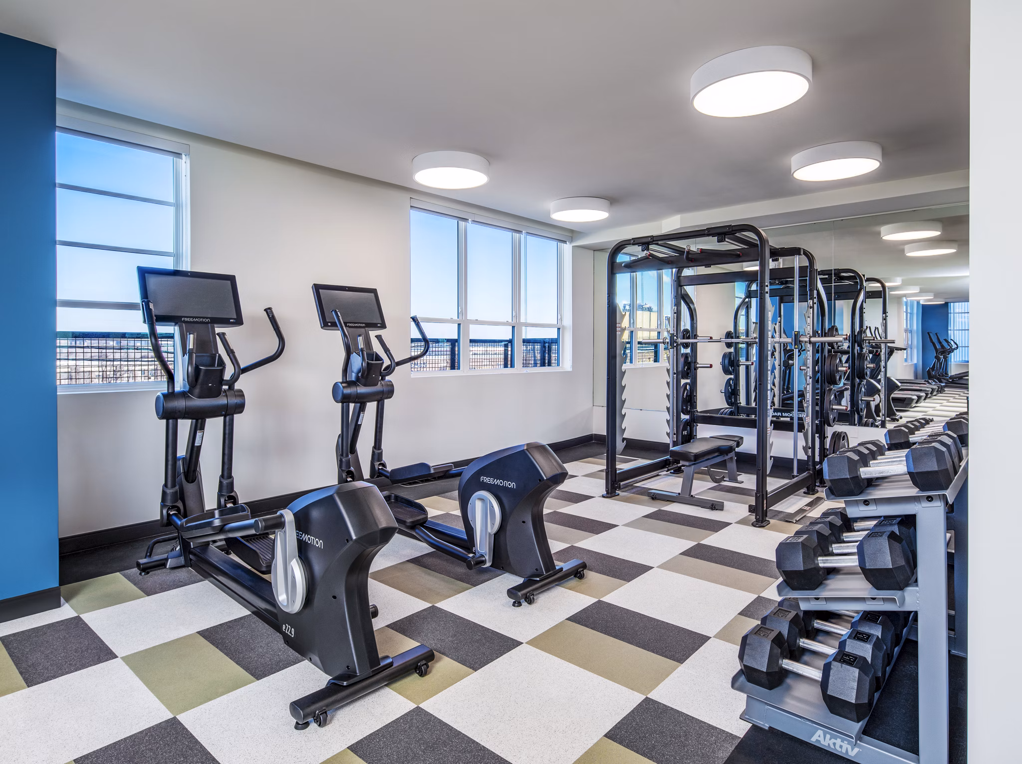 Bright and modern gym with exercise machines, weights, and large windows at The Lucie Apartments in vibrant downtown location