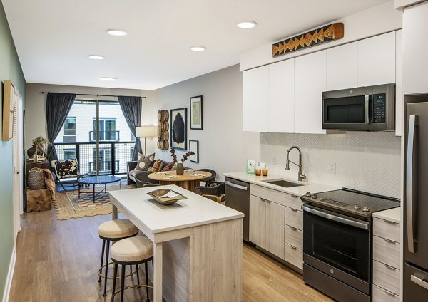 Open-concept kitchen and living room with island and barstools at The Lucie Apartments