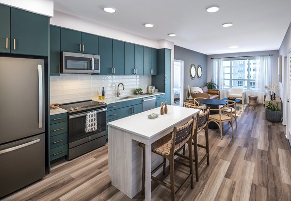 Spacious kitchen with teal cabinets, island, and open living area at The Lucie Apartments