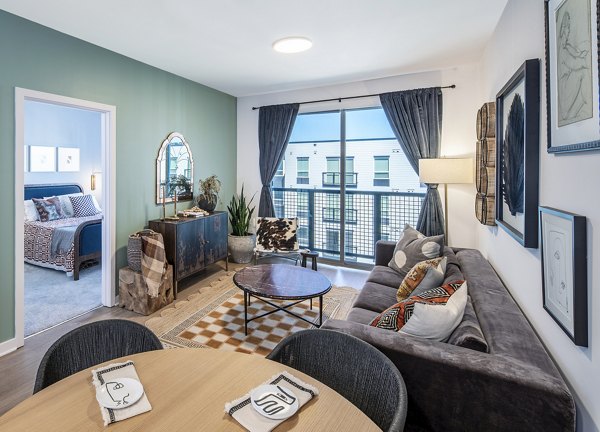 Stylish living room with gray sofa, dining table, and balcony at The Lucie Apartments