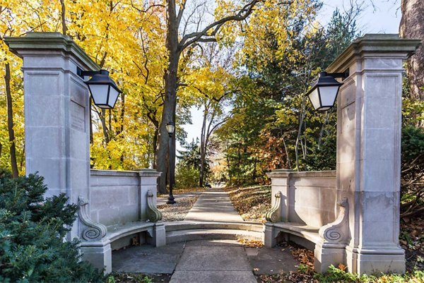 Stone entrance with pillars and lanterns leading to a tree-lined pathway with autumn foliage at luxury apartments