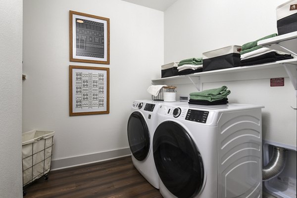 Laundry room with state-of-the-art machines and folding area in Austin Avenue Apartments