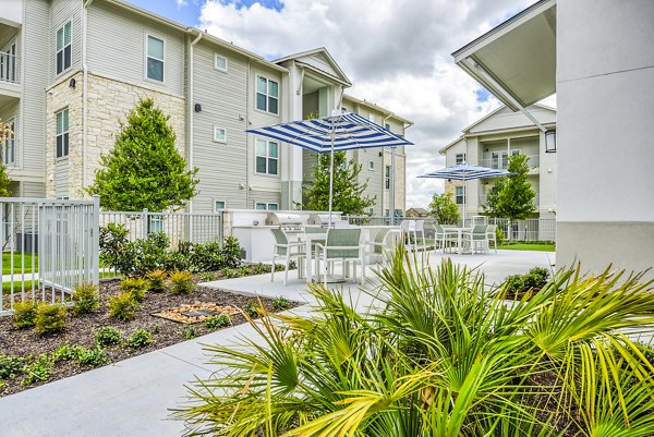 Grill area and patio at Tacara Dove Creek Apartments, featuring outdoor seating and lush landscaping