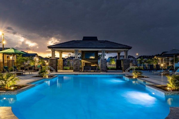 Resort-style pool at Vlux at Sunset Farms Apartments with lounge chairs and lush landscaping