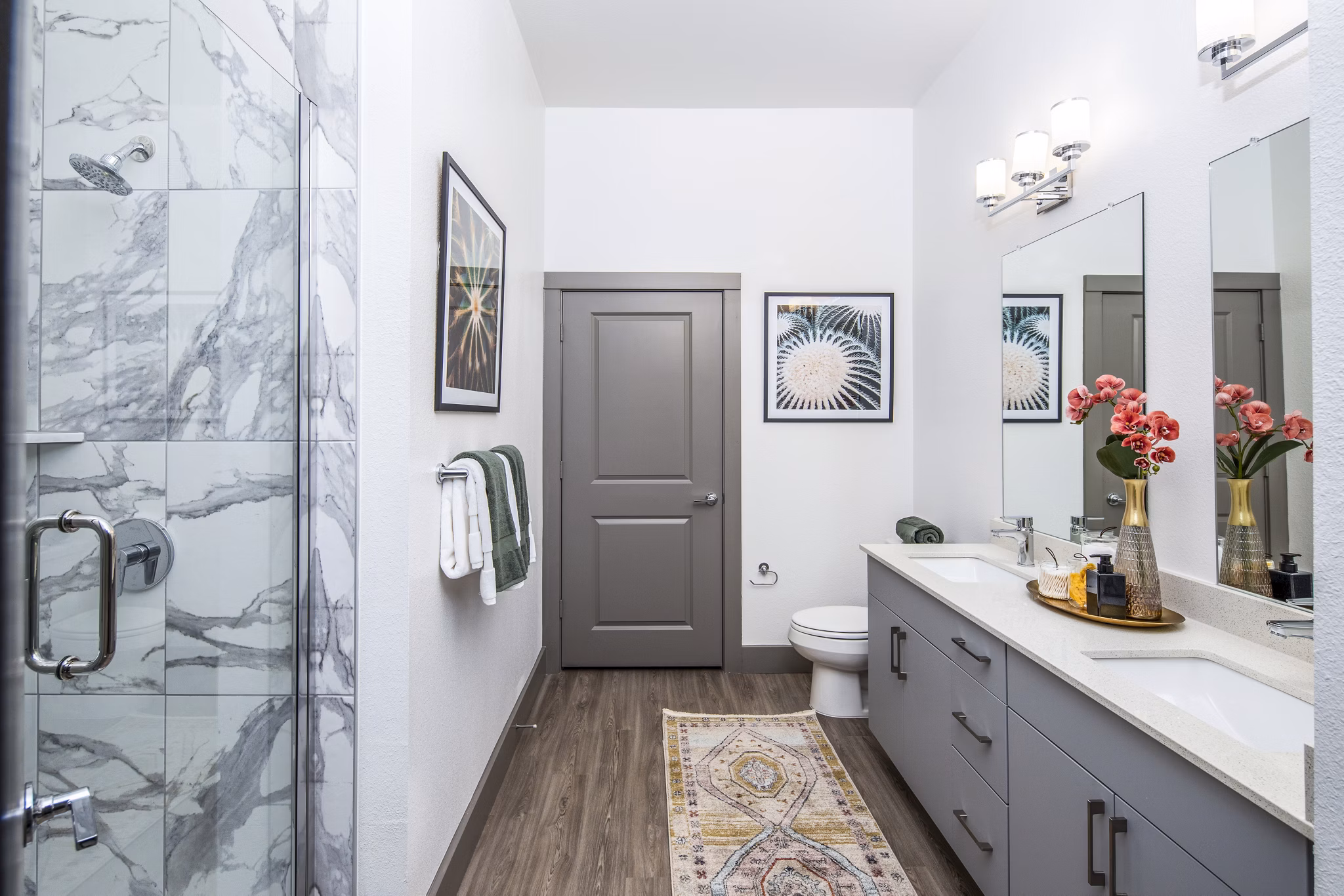 Modern bathroom featuring a double sink vanity and glass-enclosed shower with decorative artwork and flowers