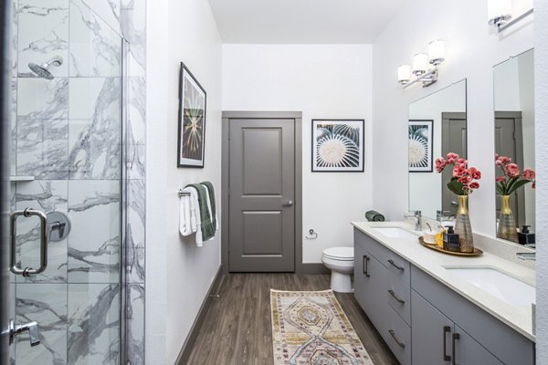 Modern bathroom featuring a double sink vanity and glass-enclosed shower with decorative artwork and flowers