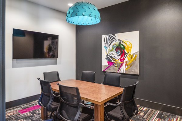 Conference room with a large table, modern chairs, and wall-mounted TV featuring colorful art and blue ceiling light
