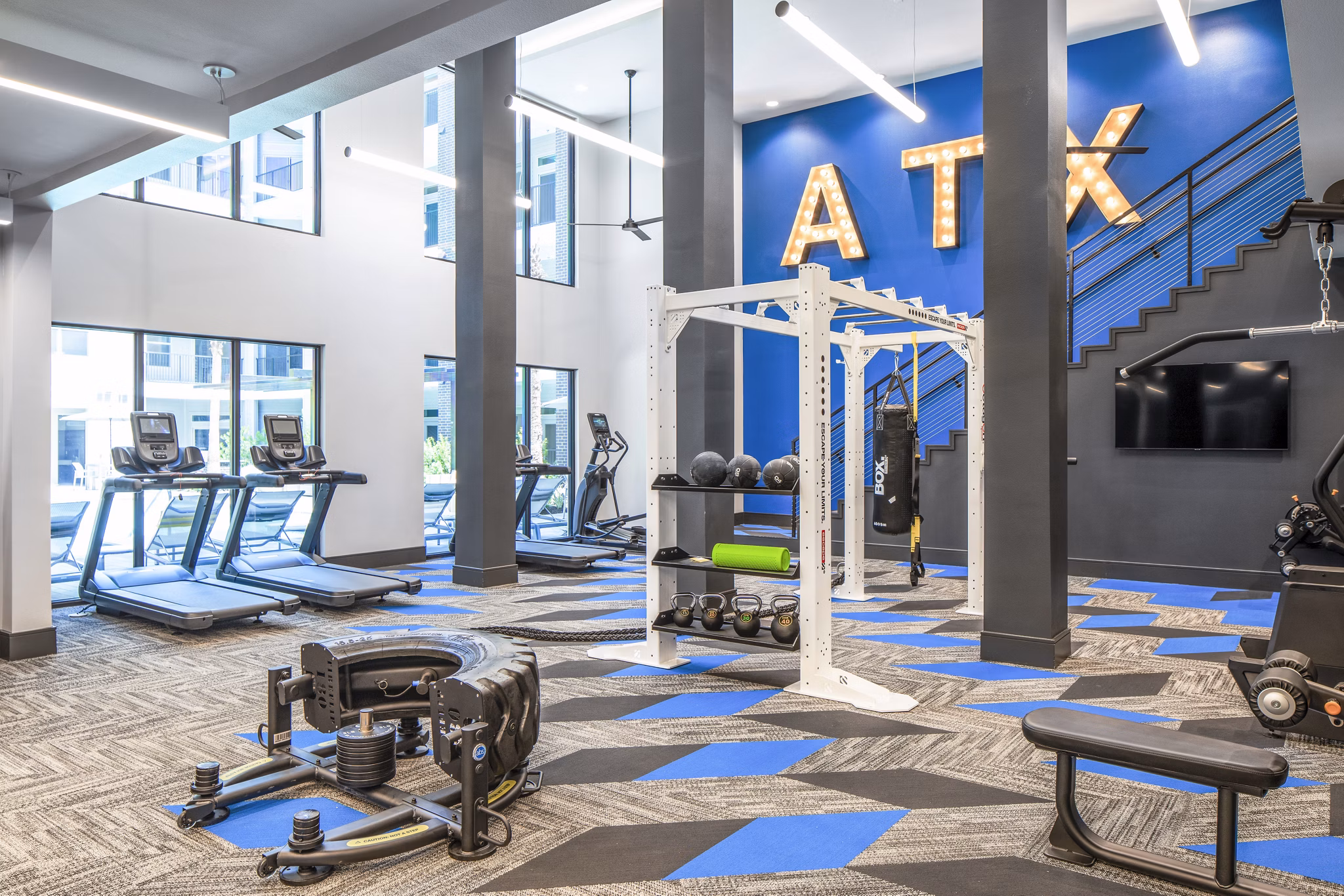 Modern gym featuring exercise equipment, including treadmills and weights, with ATX displayed on the wall