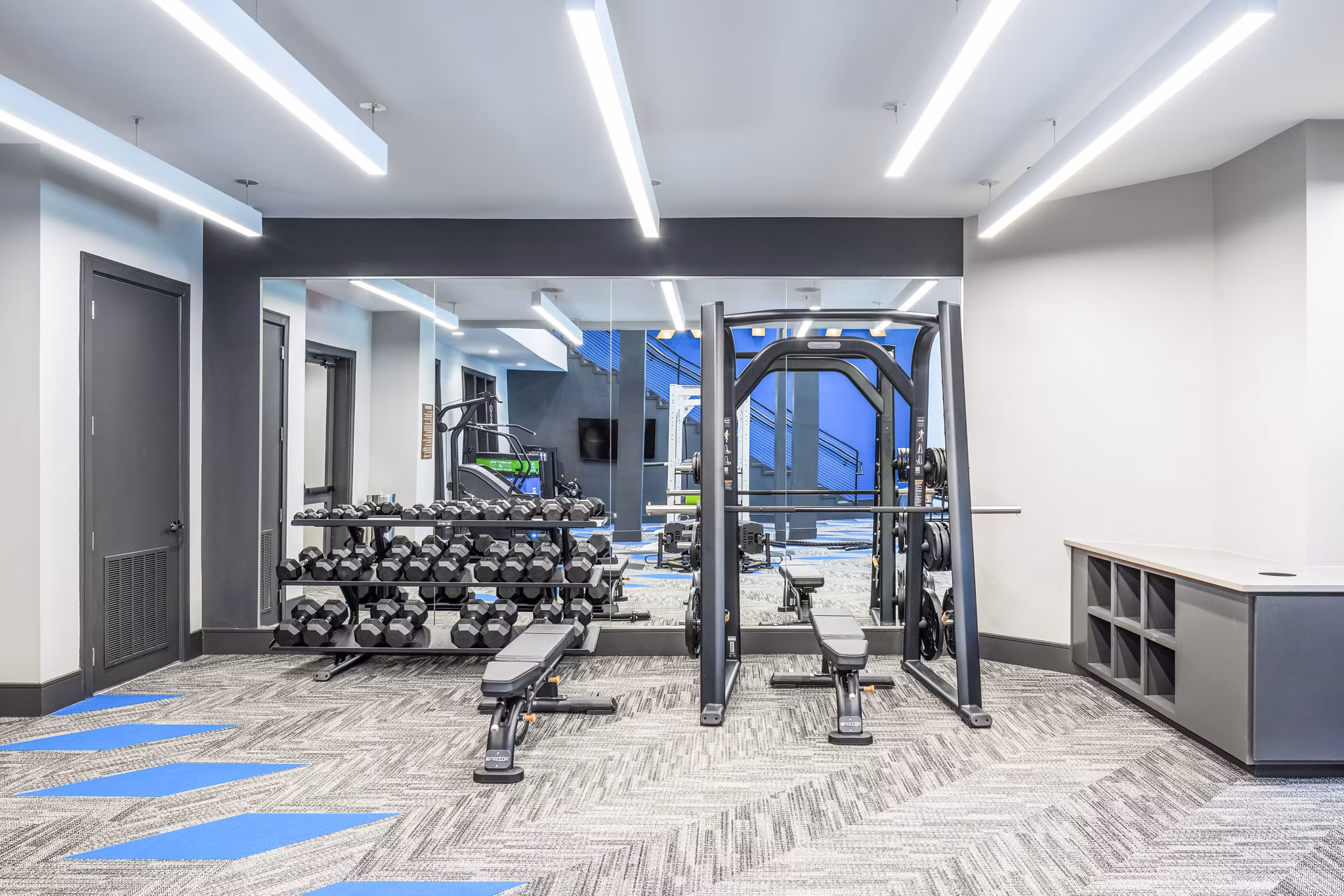 Modern gym with weight rack, dumbbells, and mirrored wall at luxury apartments