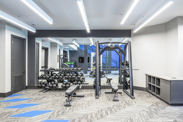 Modern gym with weight rack, dumbbells, and mirrored wall at luxury apartments