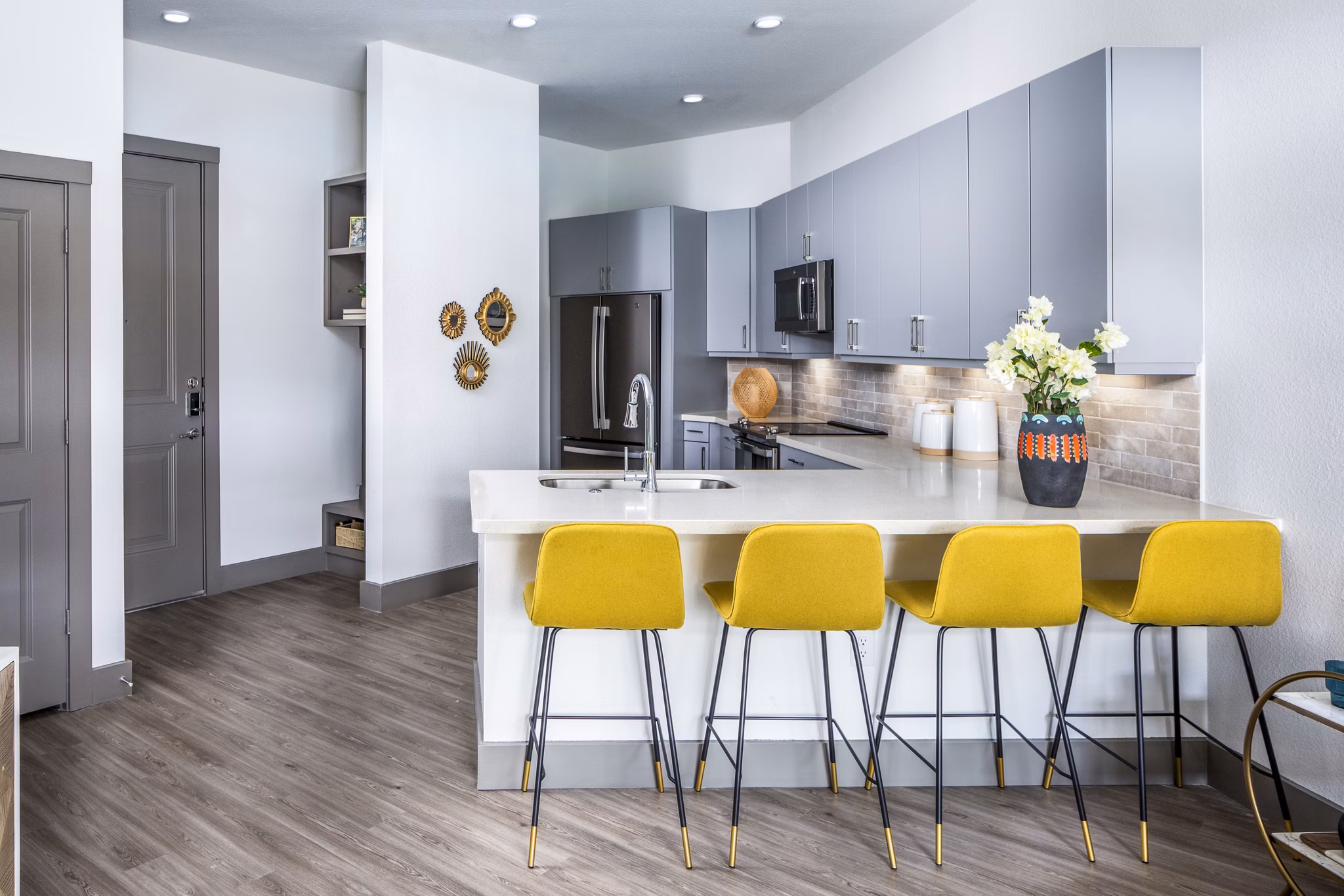 Modern kitchen with gray cabinets, white countertop, yellow bar stools, and stainless steel appliances in luxury apartments