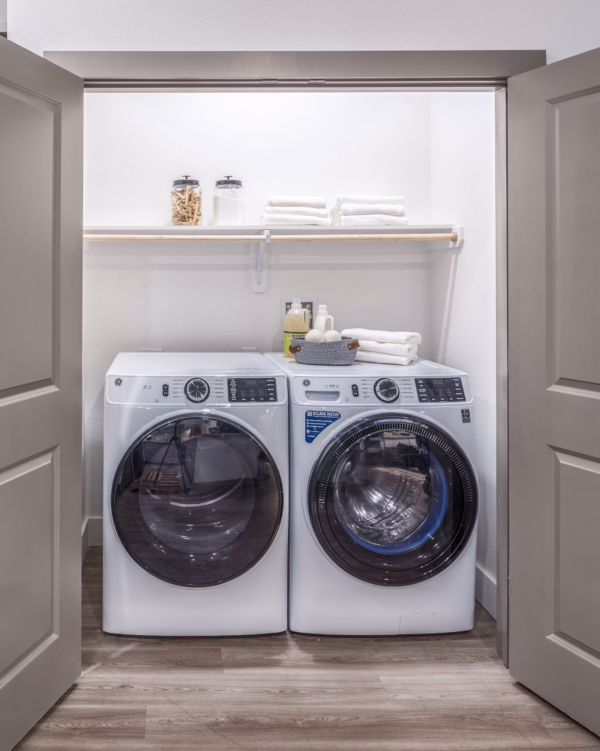 Laundry room featuring a washer, dryer, and organized shelves with folded towels and supplies in luxury apartments