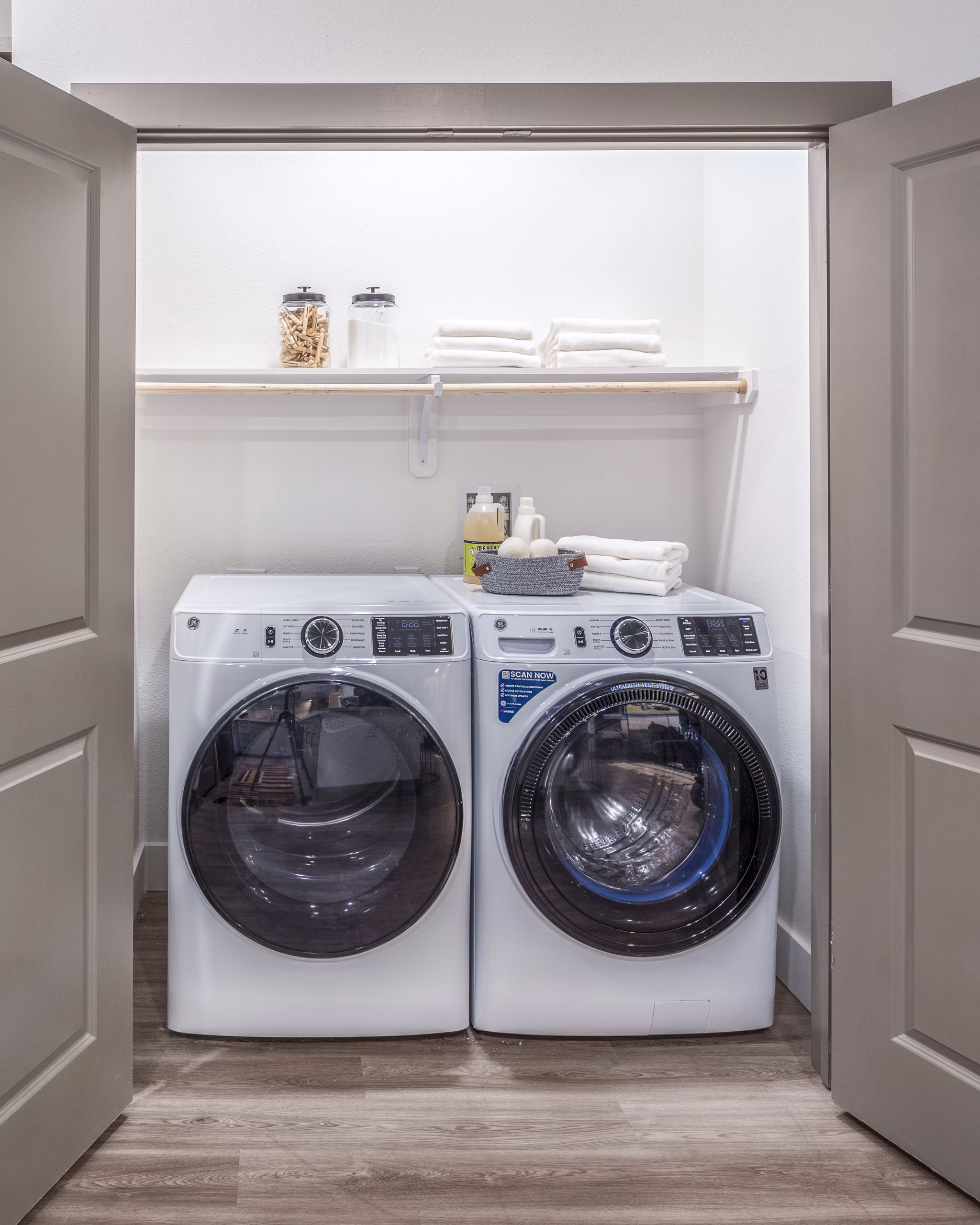 Laundry room featuring a washer, dryer, and organized shelves with folded towels and supplies in luxury apartments