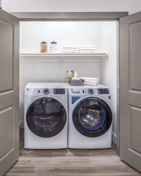 Laundry room featuring a washer, dryer, and organized shelves with folded towels and supplies in luxury apartments