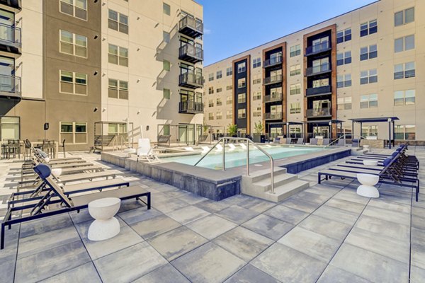 Modern pool area at Novus Apartments featuring luxury lounge chairs and lush landscaping