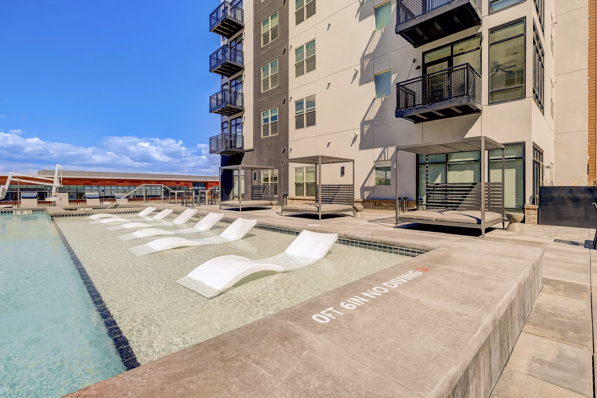Serene outdoor pool at Novus Apartments with sun loungers and lush landscaping, ideal for relaxation and leisure activities