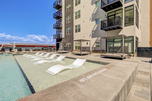 Serene outdoor pool at Novus Apartments with sun loungers and lush landscaping, ideal for relaxation and leisure activities