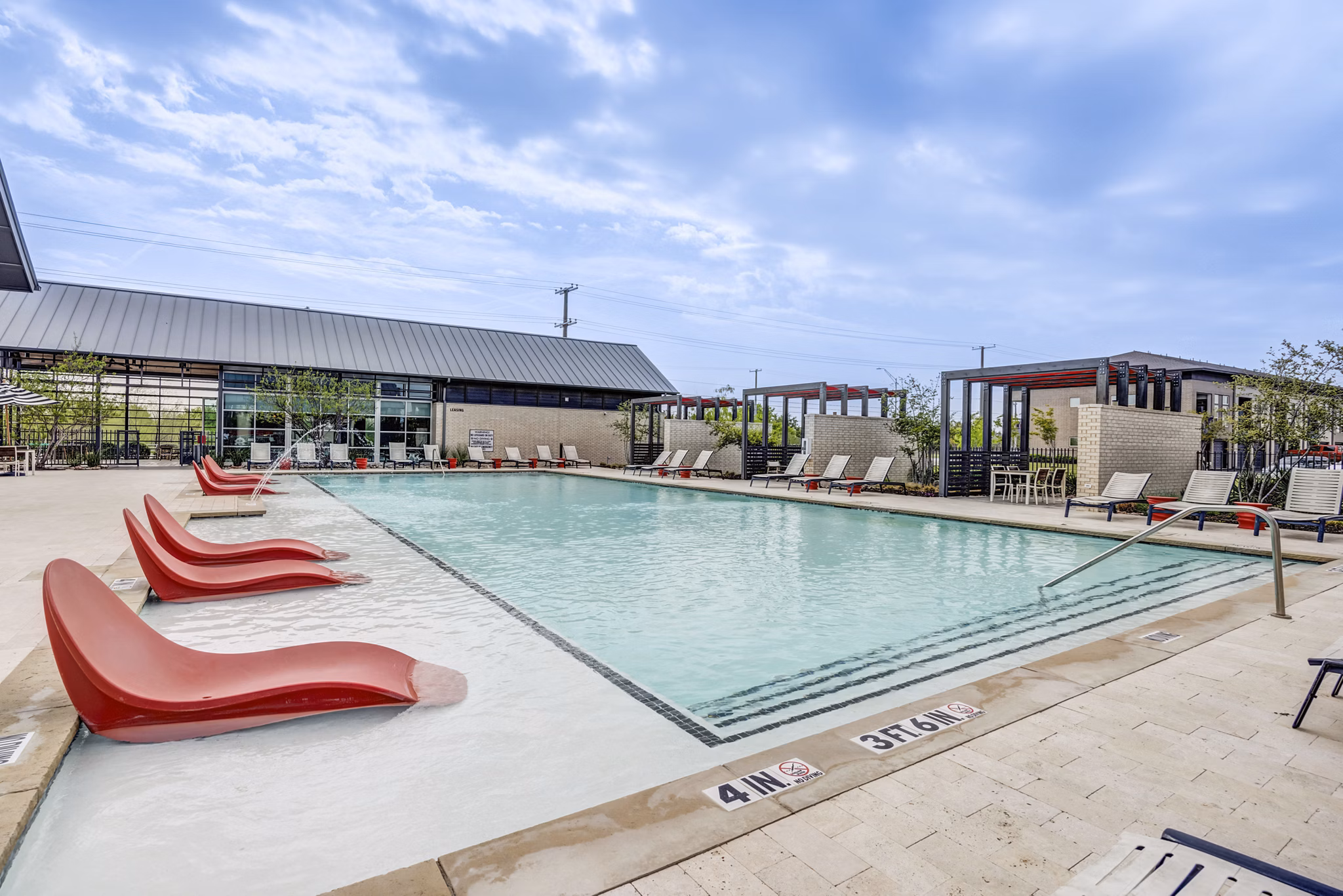 Modern outdoor pool at Parkside at Round Rock Apartments featuring lush landscaping and lounging areas