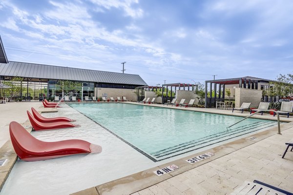 Modern outdoor pool at Parkside at Round Rock Apartments featuring lush landscaping and lounging areas