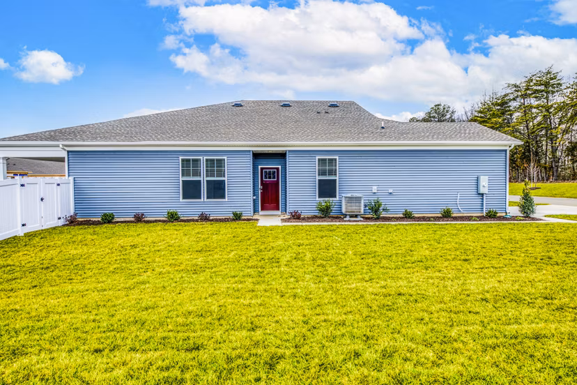 Charming single-story house with blue siding and a red door in a lush grassy yard