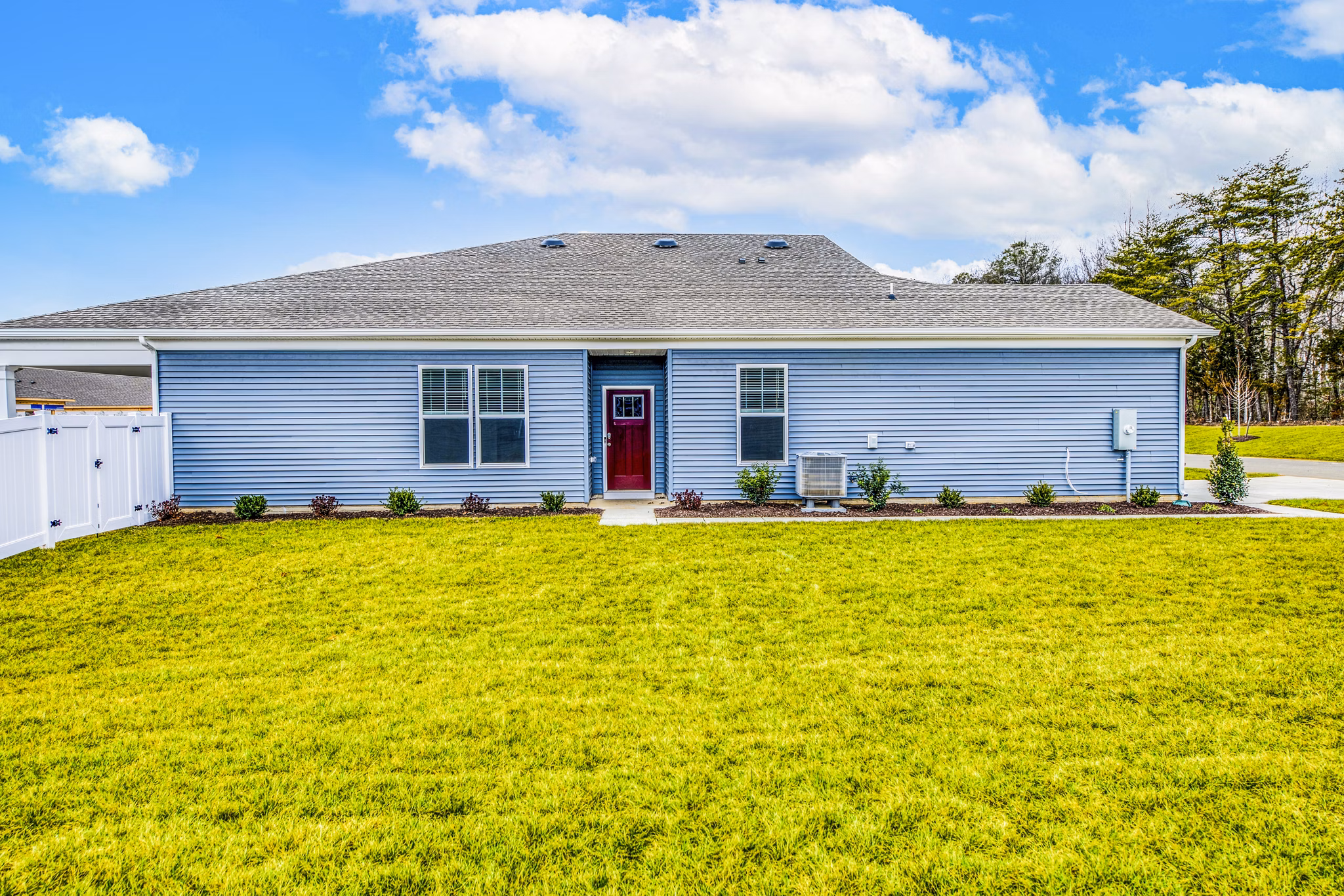Charming single-story house with blue siding and a red door in a lush grassy yard